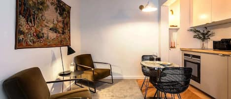 Una sala moderna con un sofá, una mesa de centro y una mesa de comedor con sillas. Hay un cuadro en la pared, una lámpara y una zona de cocina con armarios y encimera.