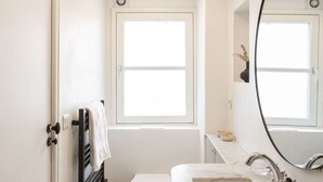 Uma casa de banho moderna com sanita branca, lavatório com bancada de mármore, espelho grande e janela que proporciona luz natural.