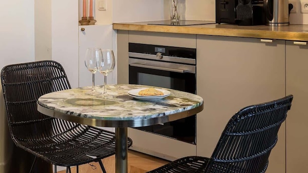 Cozinha moderna com armários brancos, uma mesa redonda com cadeiras, uma cafeteira e um vaso com plantas.