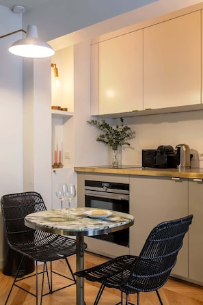 A modern kitchen with white cabinets, a round table with chairs, a coffee machine, and a vase with plants.