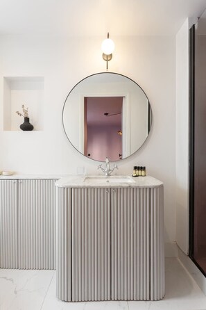 A modern bathroom with a round mirror, a white vanity, and a light fixture above the mirror.