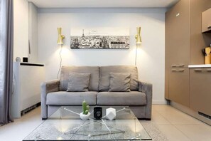 A modern living room with a sofa, a glass coffee table, and a cityscape painting on the wall.