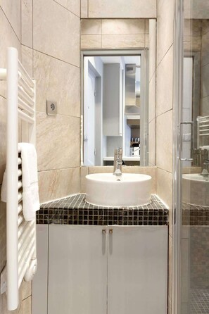 Un baño moderno con un lavamanos blanco, una cabina de ducha de vidrio y suelo de baldosas.