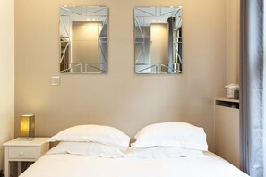 Una habitación de hotel con una cama, dos espejos en la pared, una mesita de noche y una lámpara.