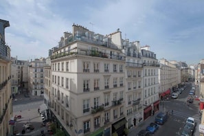 A multi-story building with balconies, a street in front, and parked cars.