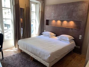 A bedroom with a large bed, a headboard with built-in lighting, a window with curtains, and a view of the outside. - Cosy studio in the heart of le Marais - A/C - Steps from the Pompidou Centre - Marais Sicile I by Habitat Parisien (Paris)