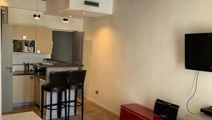 A modern room with a large bed, a kitchen area with bar stools, and a TV mounted on the wall. - Cosy studio in the heart of le Marais - A/C - Steps from the Pompidou Centre - Marais Sicile I by Habitat Parisien (Paris)