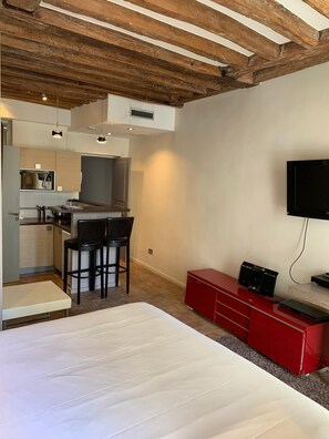 A modern room with a large bed, a kitchen area with bar stools, and a TV mounted on the wall.