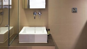 Ein modernes Badezimmer mit einer Glaskabine zur Dusche, einem weißen Waschbecken mit Spiegel darüber und einer Toilette auf der rechten Seite.
