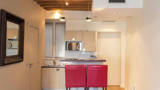 A compact kitchen with a microwave, a sink, and a small island with red bar stools. - Cosy studio in the heart of le Marais - A/C - Steps from the Pompidou Centre - Marais Sicile I by Habitat Parisien (Paris)