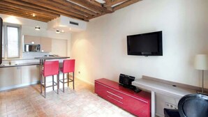 A modern kitchen with a bar area, a flat-screen TV, and a red cabinet. - Cosy studio in the heart of le Marais - A/C - Steps from the Pompidou Centre - Marais Sicile I by Habitat Parisien (Paris)