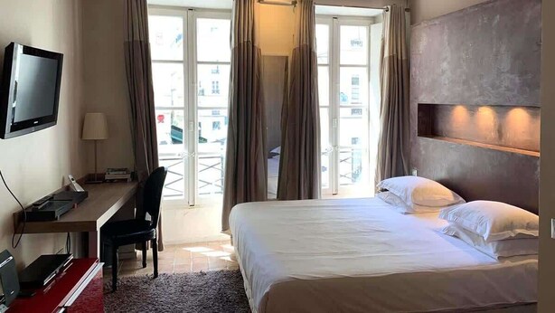 Ein Hotelzimmer mit Bett, Schreibtisch, Fernseher und einem Balkon mit Vorhängen.