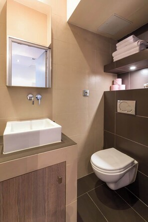 A modern bathroom with a rectangular sink, a mirror, a toilet, and a towel rack.