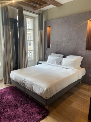 Una camera da letto moderna con un letto grande, un tappeto viola e una finestra con tende.