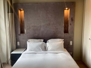 Una camera d'albergo moderna con un letto grande, due luci fissate al muro e un parete spoglia.