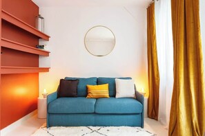 Een moderne woonkamer met een blauwgroene bank, een ronde spiegel en een gouden gordijn.