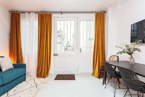 Ein Zimmer mit einer Couch, einem Esstisch mit Stühlen und einer Tür mit Vorhängen.