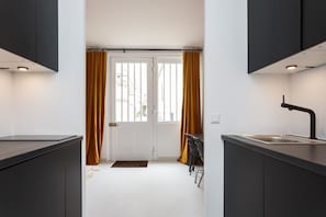 A modern kitchen with dark cabinetry, a black countertop, a sink, and a window with curtains.