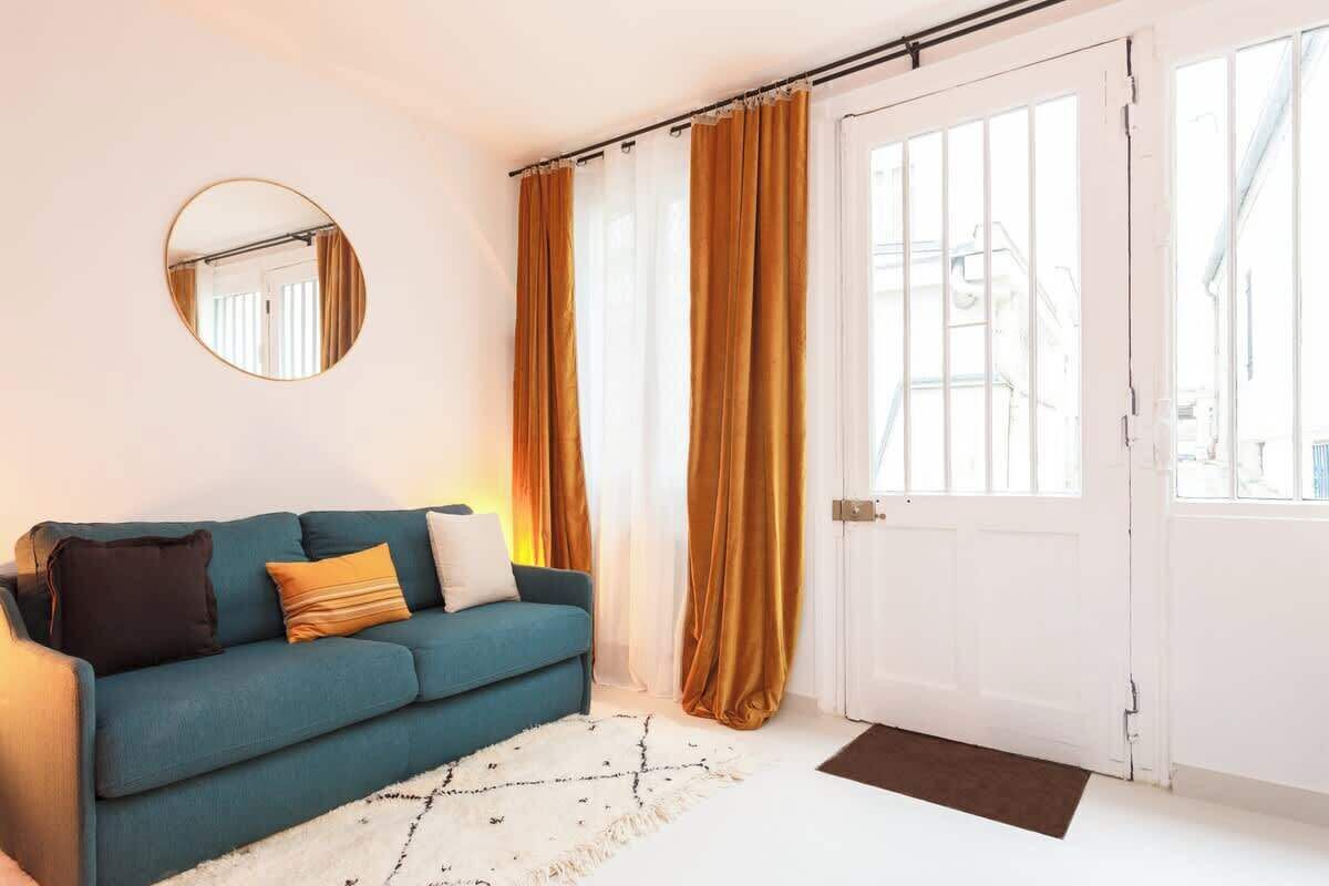 A room with a teal sofa, a round mirror, and a white door with a view of the outside.