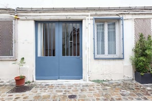 Ein Gebäude mit einer blauen Tür, einem Fenster mit Metallgitter und einem Blumentopf.