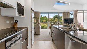 Una cocina moderna con una isla grande, electrodomésticos integrados y vistas a un jardín exuberante a través de amplios ventanales.