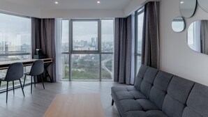 A modern living room with a large sofa, a dining table with chairs, and a view of a cityscape through floor-to-ceiling windows. - HOTEL LUURE  (Huixquilucan)