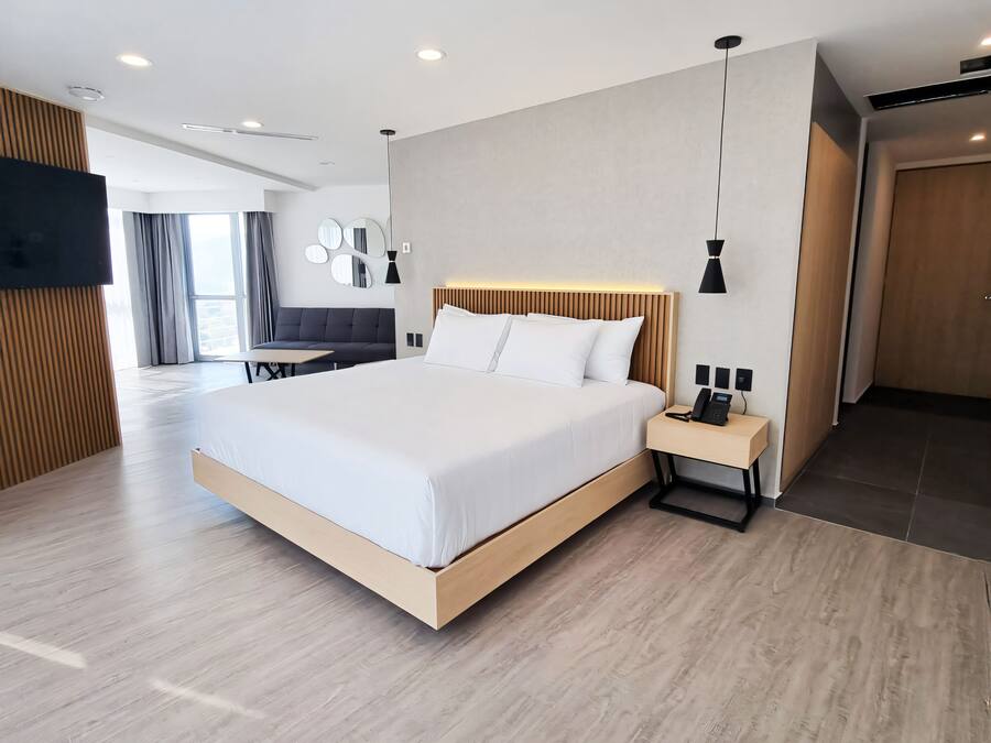 A modern hotel room with a large bed, bedside table, and a TV mounted on the wall.