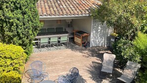 Un patio al aire libre cubierto con techo de baldosas, rodeado de follaje y un muro de piedra.