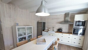 Una cocina moderna con armarios blancos, un refrigerador de acero inoxidable, horno empotrado y una lámpara colgante.