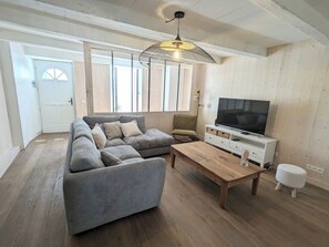 A living room with a grey sectional sofa, a wooden coffee table, a television on a white cabinet, and a hanging light fixture. - L'escale Révée - 6 people (La Flotte)