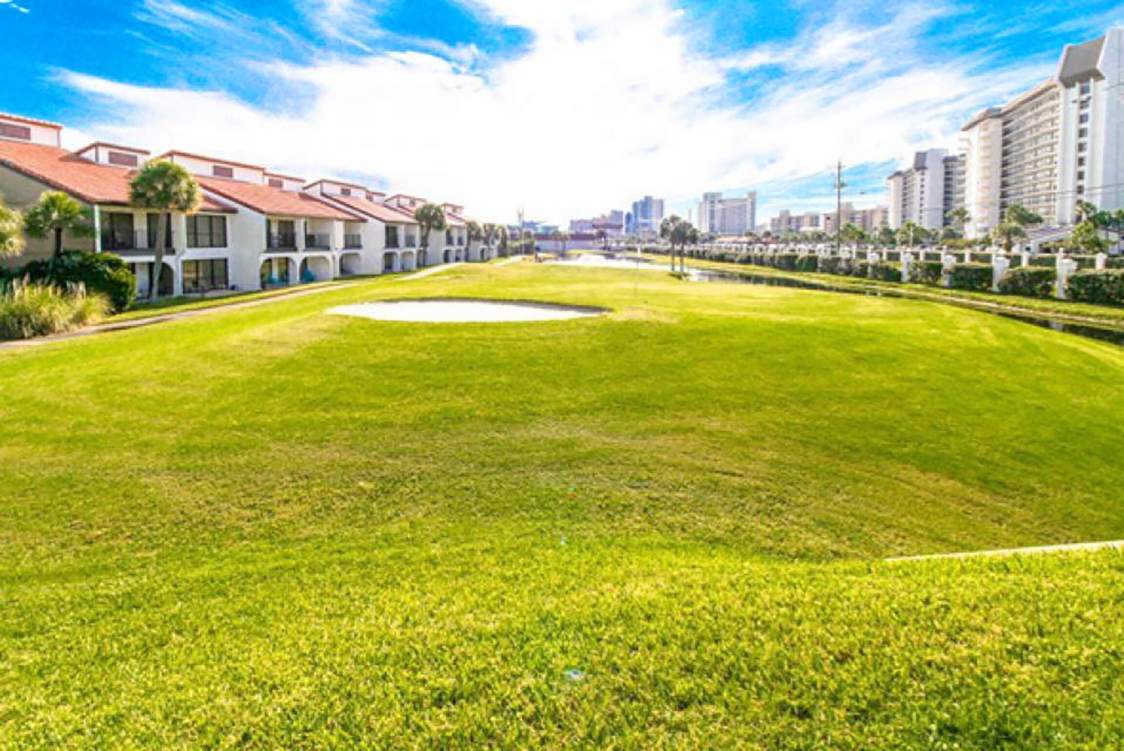 A well-maintained grassy area with a small pond, surrounded by multi-story buildings with balconies.