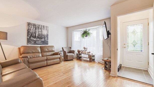 A living room with a sofa, armchair, and a coffee table with plants. There is a door with a glass panel and a painting on the wall. - Le Cardinal Moderne-Wi-Fi rapide. Family-sized all included! (Laval)
