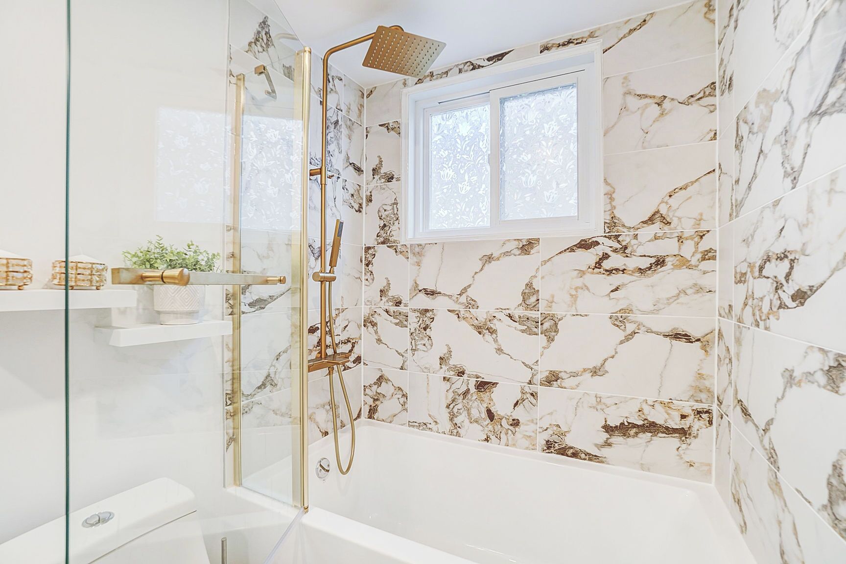 Une salle de bain avec une douche à parois de verre, une baignoire blanche, des murs à motifs de marbre et une petite fenêtre.