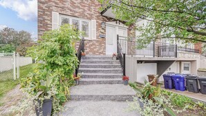 A brick building with a set of concrete stairs leading to a white door. There are potted plants along the stairs and a metal fence in the background. - Le Cardinal Moderne-Wi-Fi rapide. Family-sized all included! (Laval)
