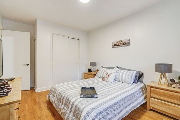 A bedroom with a bed, bedside tables, a nightstand, a door, and a wall-mounted picture. - Le Cardinal Moderne-Wi-Fi rapide. Family-sized all included! (Laval)