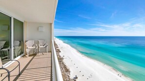Ein Balkon mit Korbstühlen mit Blick auf einen Strand mit klarem türkisblauem Wasser und einem weißen Sandstrand.