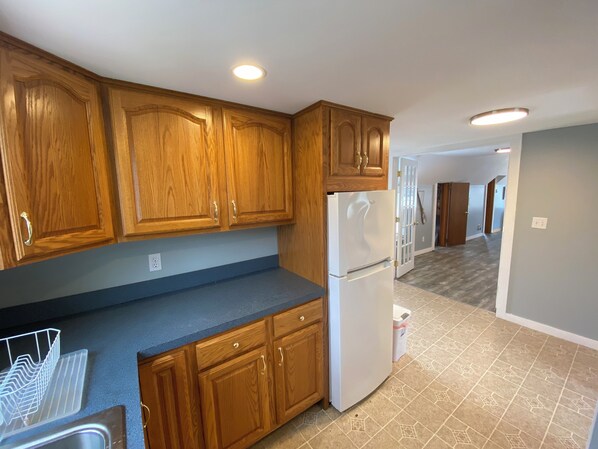 A kitchen with wooden cabinets, a white refrigerator, and a blue countertop. - Beachfront Bliss , Inviting 3 bedroom + loft at Hawks Nest Beach! (Old Lyme)