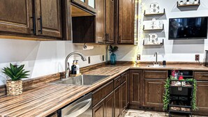 Una cocina con armarios de madera, lavavajillas integrado, piso de baldosas de piedra y un televisor montado en la pared.
