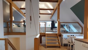 A spacious loft with a wooden staircase, a mezzanine level, and a view of the outdoors. - The Village Island - Över de Deel (Trebel)