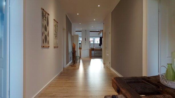 A hallway with wooden flooring, white walls, and a wooden bench with a hammer and green vase. - The Village Island - Över de Deel (Trebel)