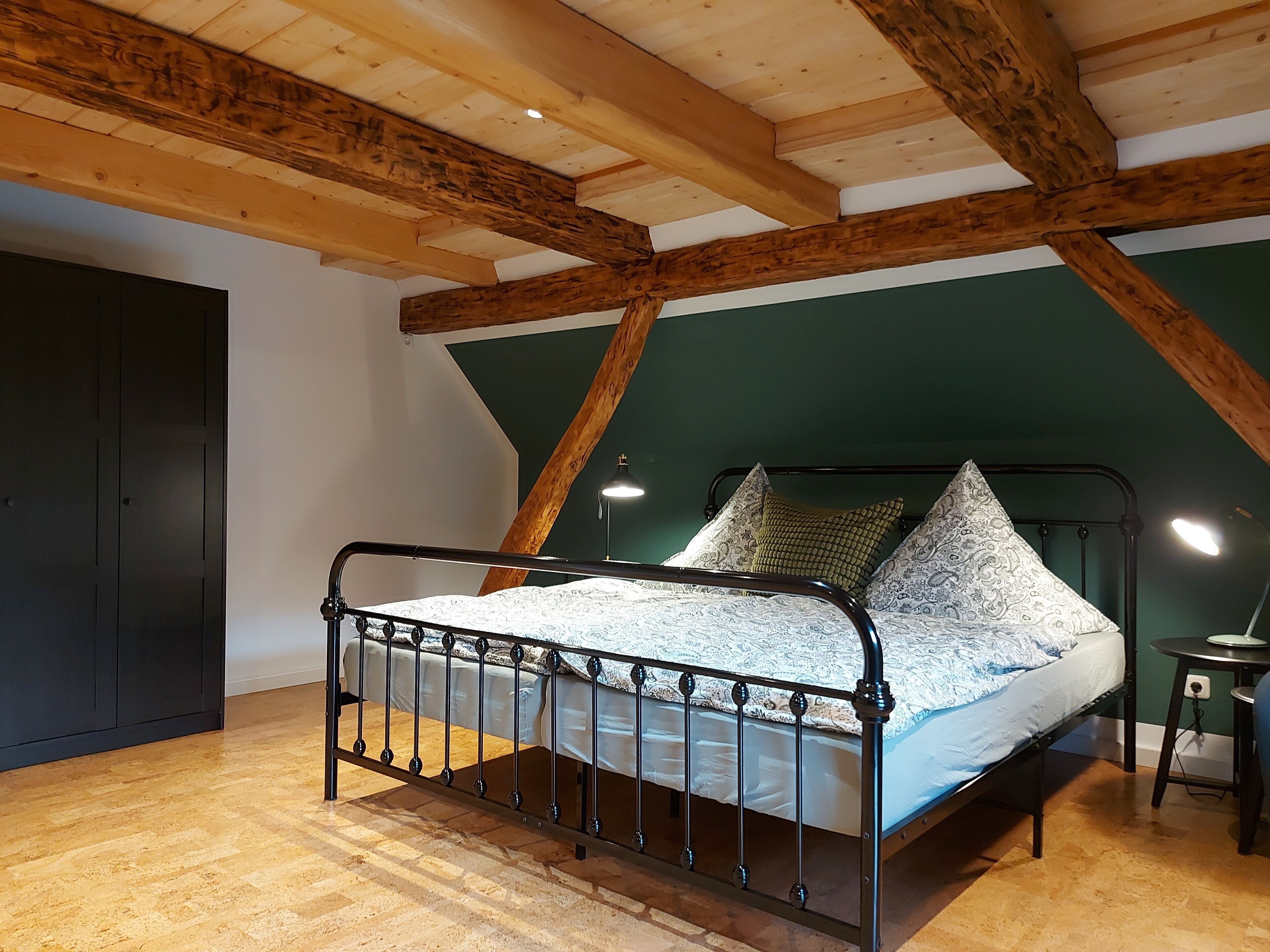 A room with a bed, wooden beams, a green wall, and a wooden floor.