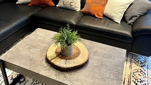 Ein modernes Wohnzimmer mit einem schwarzen Ledersofa, einem Couchtisch mit Pflanze und einem gemusterten Teppich.
