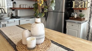 Eine Küche mit einer weißen Vase, die gelbe Blumen, eine Kerze und eine gewebte Tischmatte auf der Arbeitsfläche enthält.