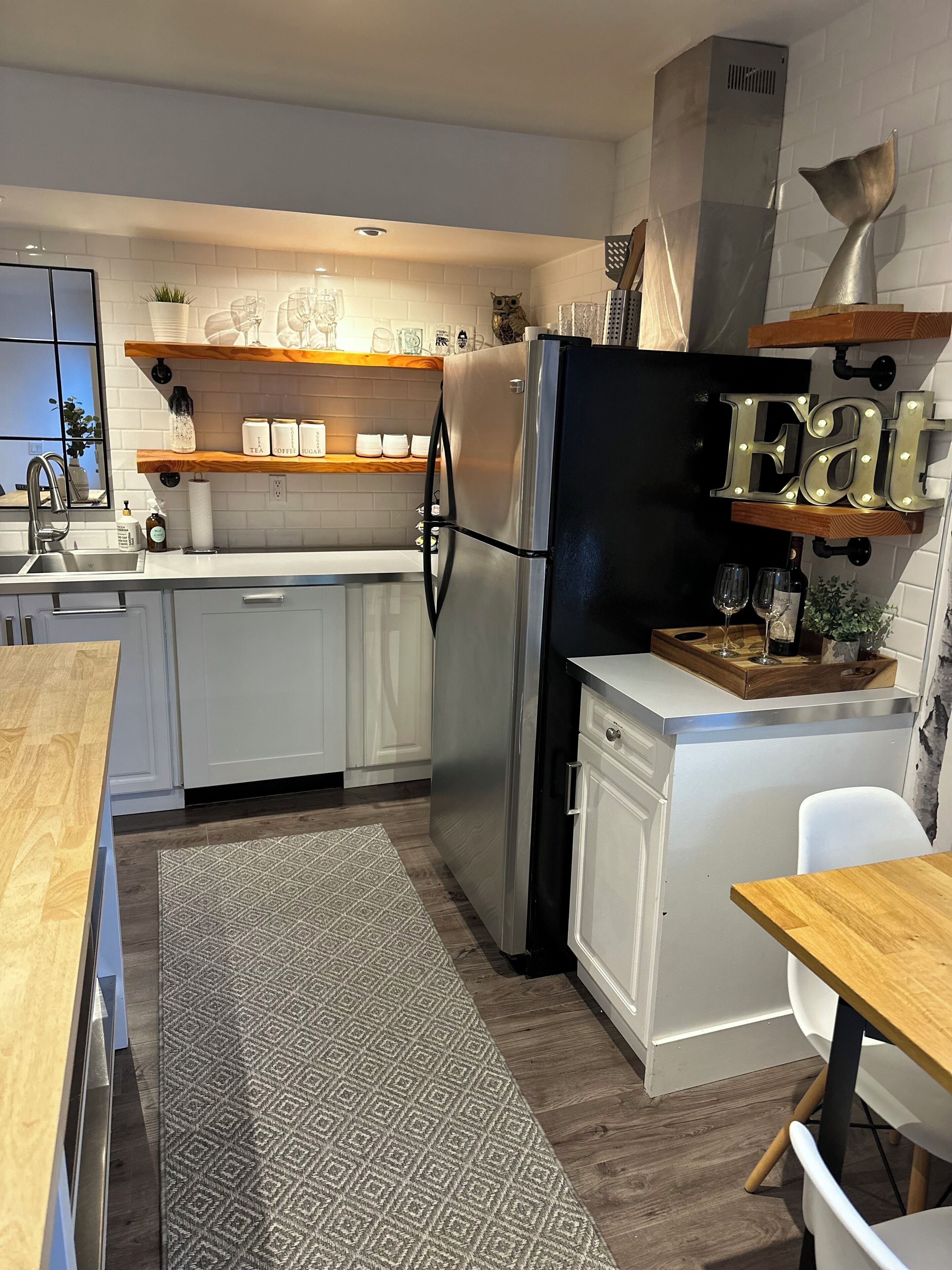 A modern kitchen with white cabinets, a stainless steel refrigerator, a wooden countertop, and a built-in oven.