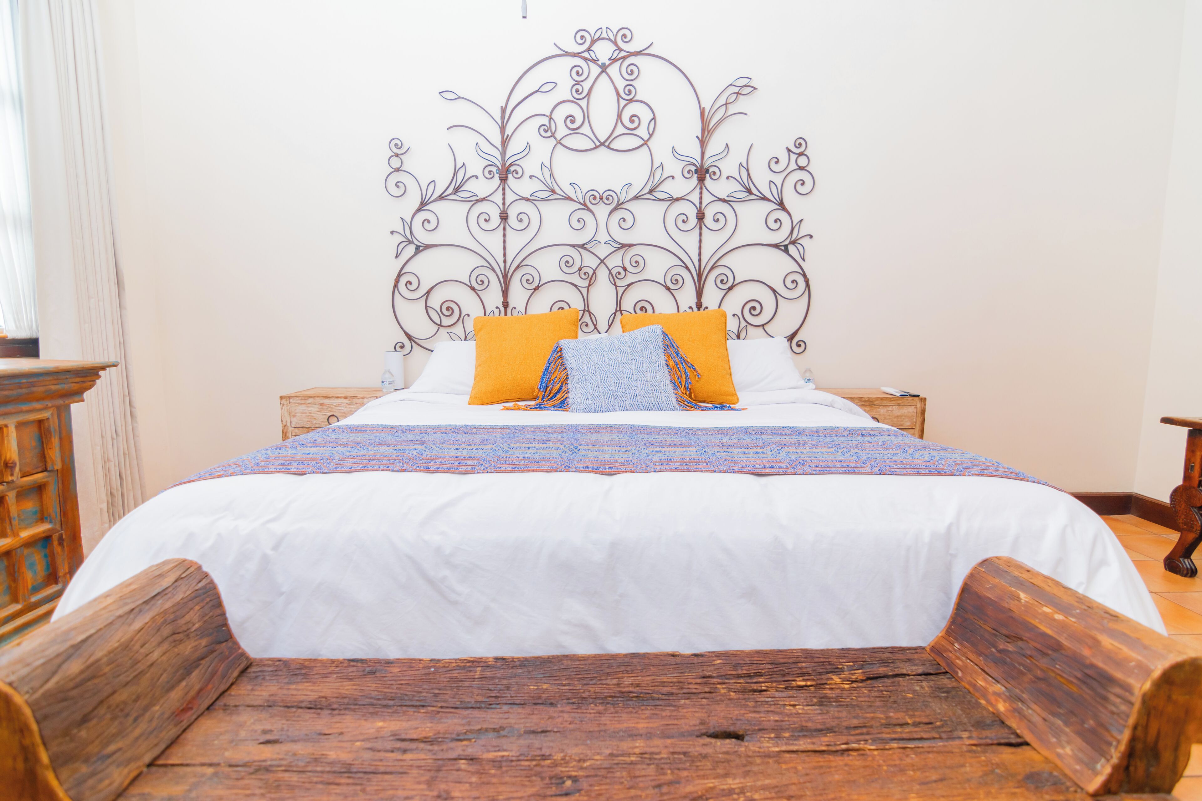 A bed with a white bedspread, two orange pillows, and a decorative headboard.