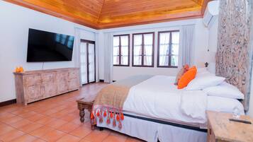 A bedroom with a large bed, a wooden ceiling, a TV mounted on the wall, and a stone wall.