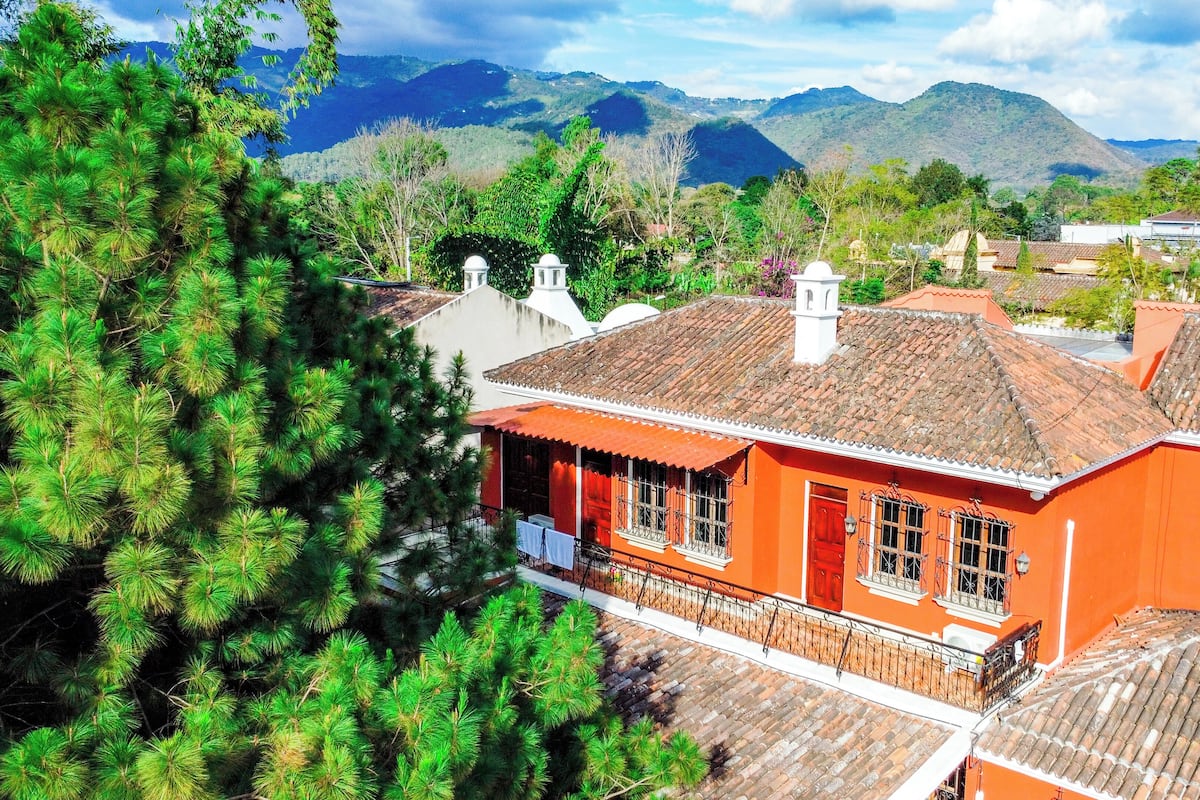 A traditional building with a tiled roof, surrounded by lush greenery and mountains in the background.