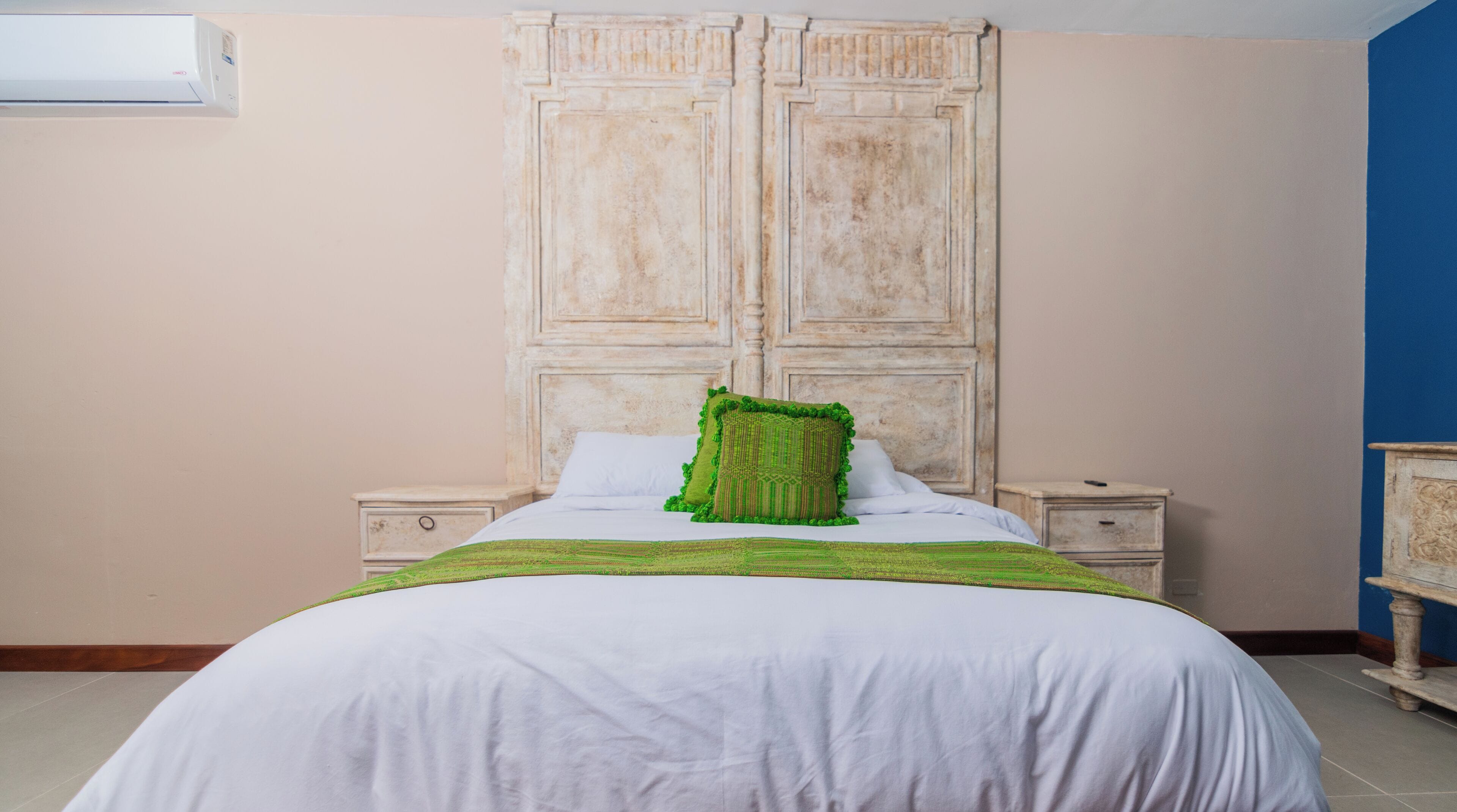 A bedroom with a large bed, two bedside tables, a wardrobe, and an air conditioning unit.