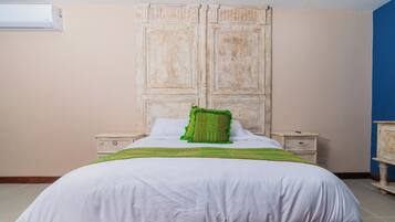 A bedroom with a large bed, two bedside tables, a wardrobe, and an air conditioning unit.