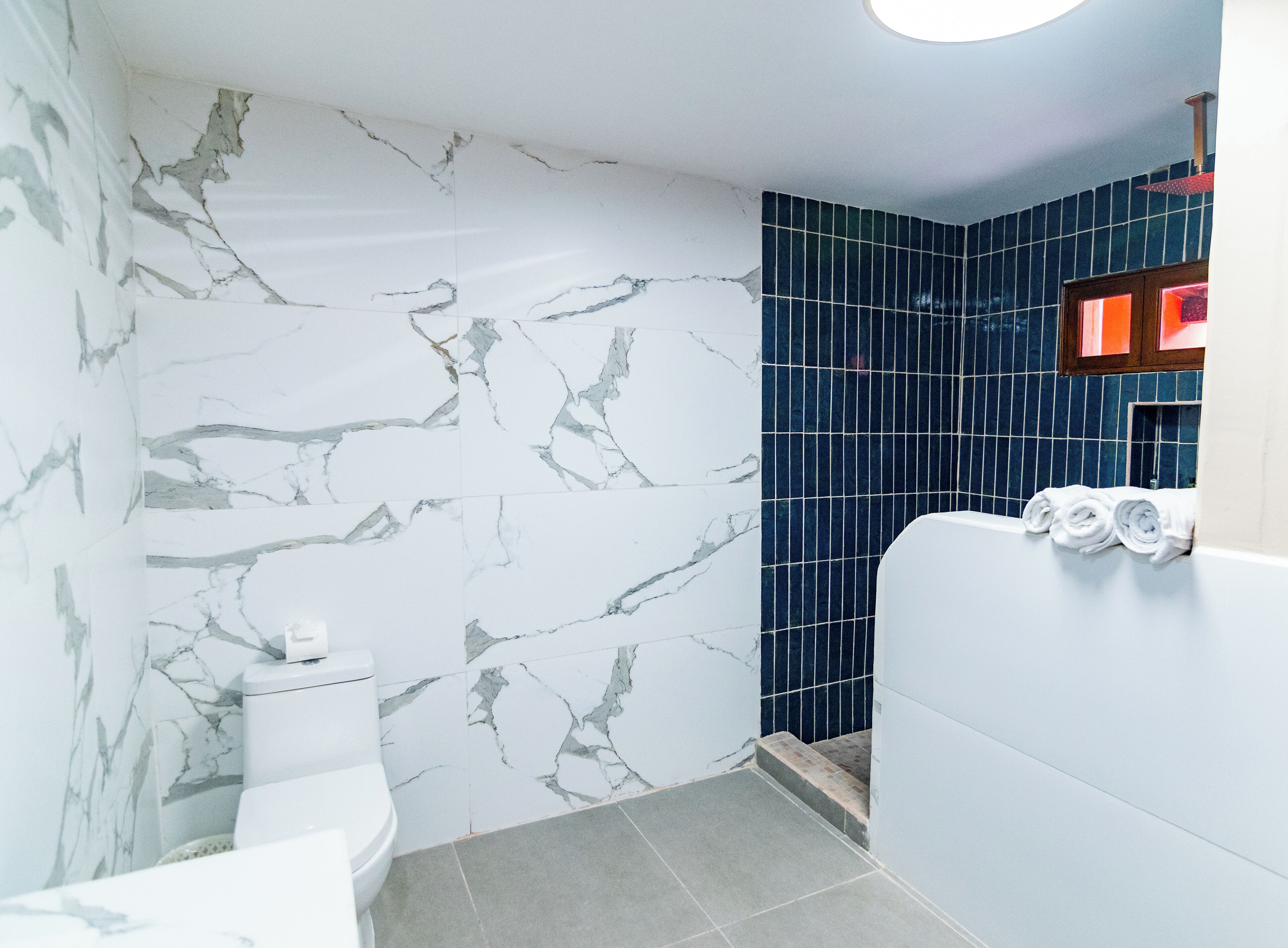 Une salle de bain avec des murs en marbre blanc, une douche carrelée de carreaux bleus et des toilettes.